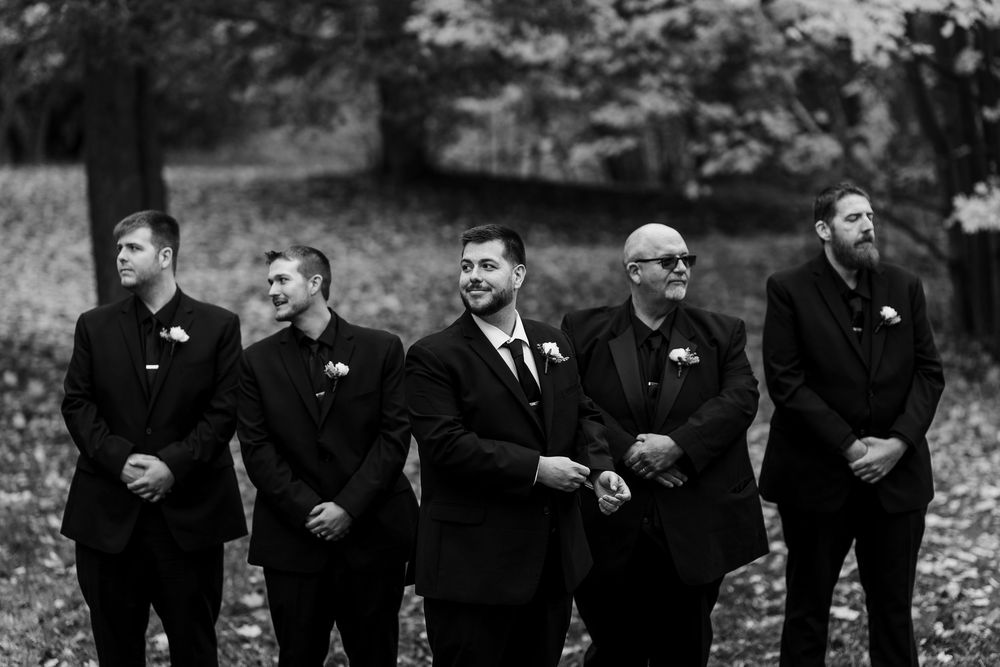 Groomsmen in black suits line up for a fun photo in a black and white setting.