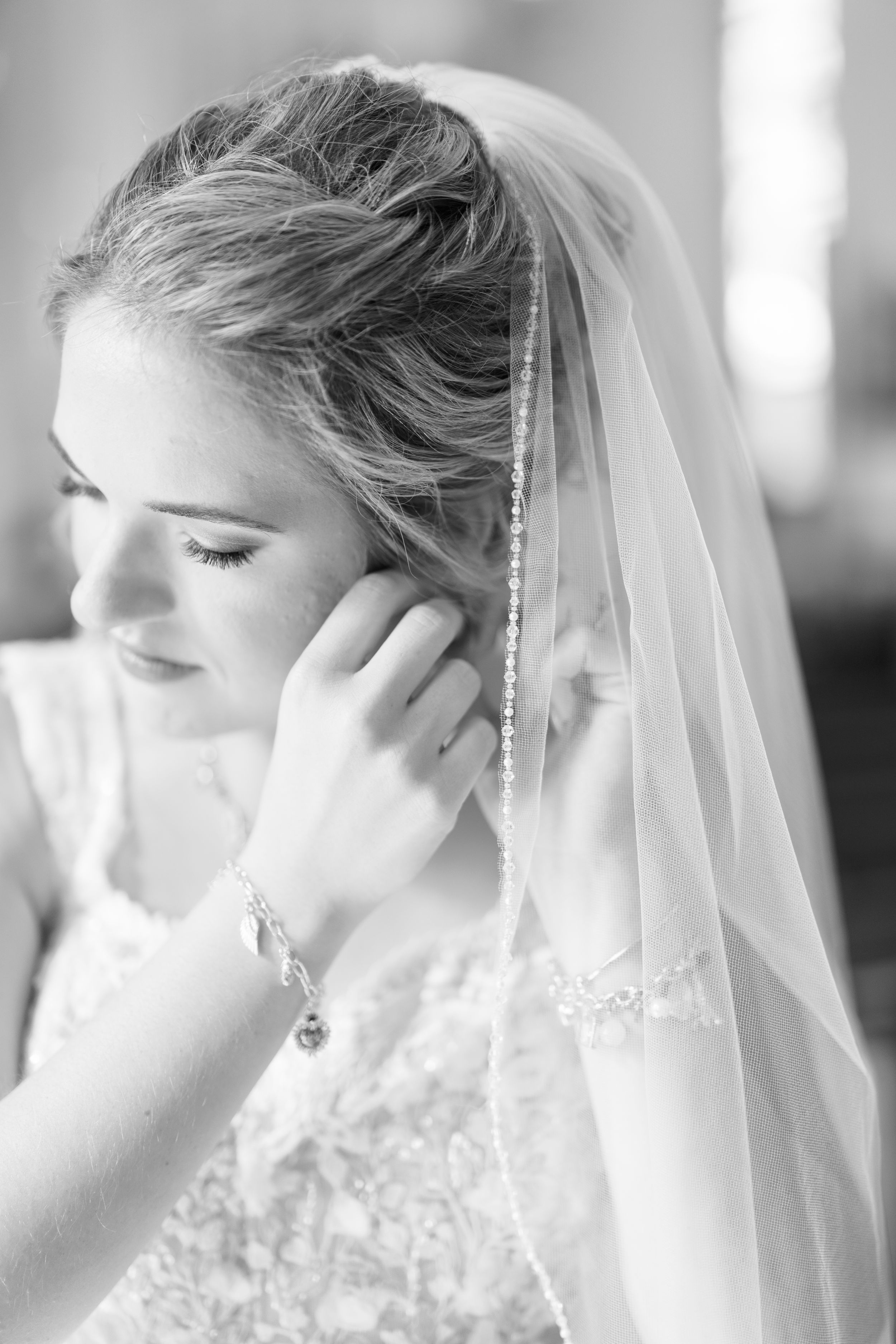 Elegant black and white bridal portrait showing delicate lace dress and flowing veil with beaded detail.