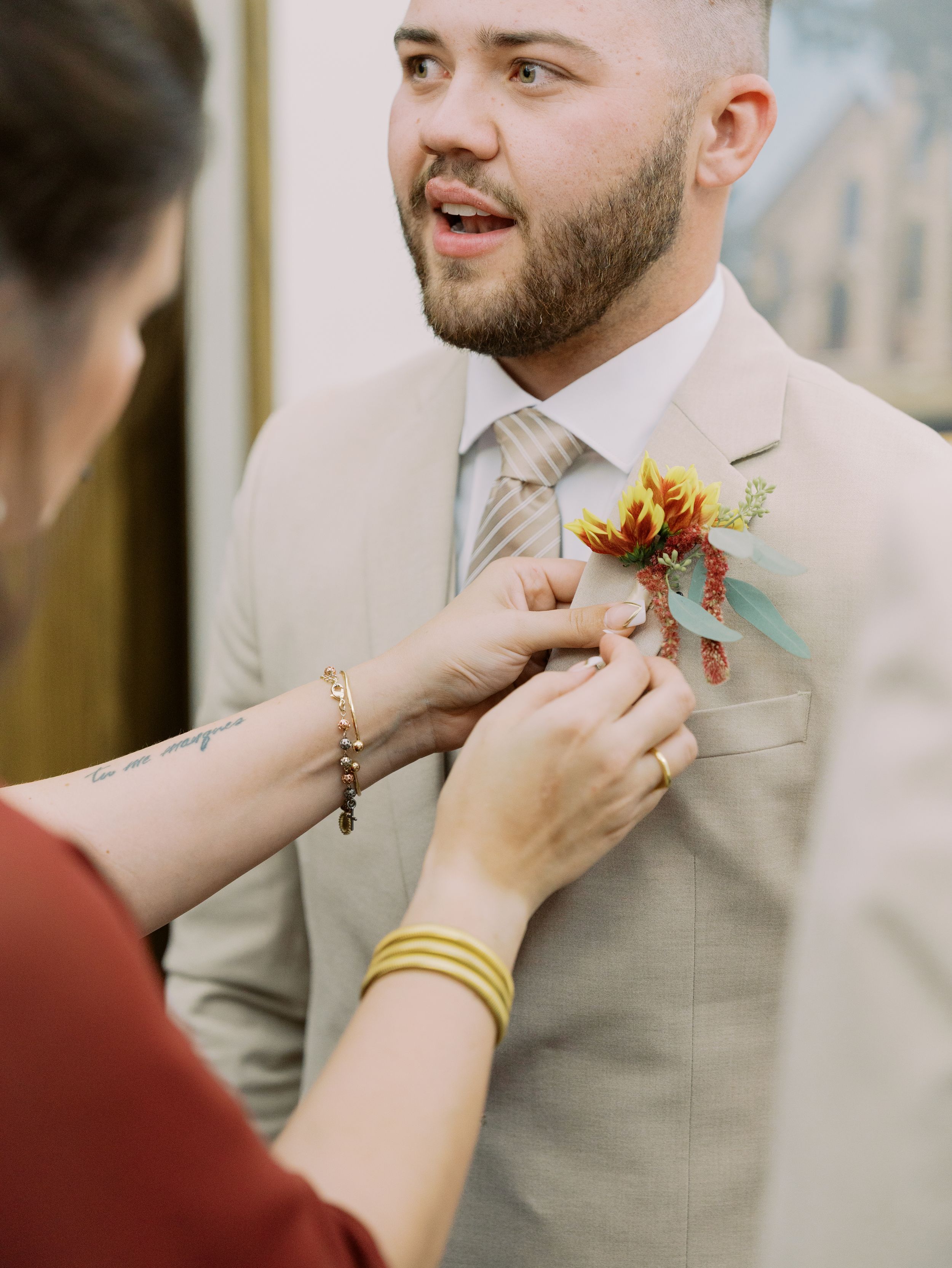 A boutonniere being pinned onto a light beige suit jacket in a sequence of closeup shots.
