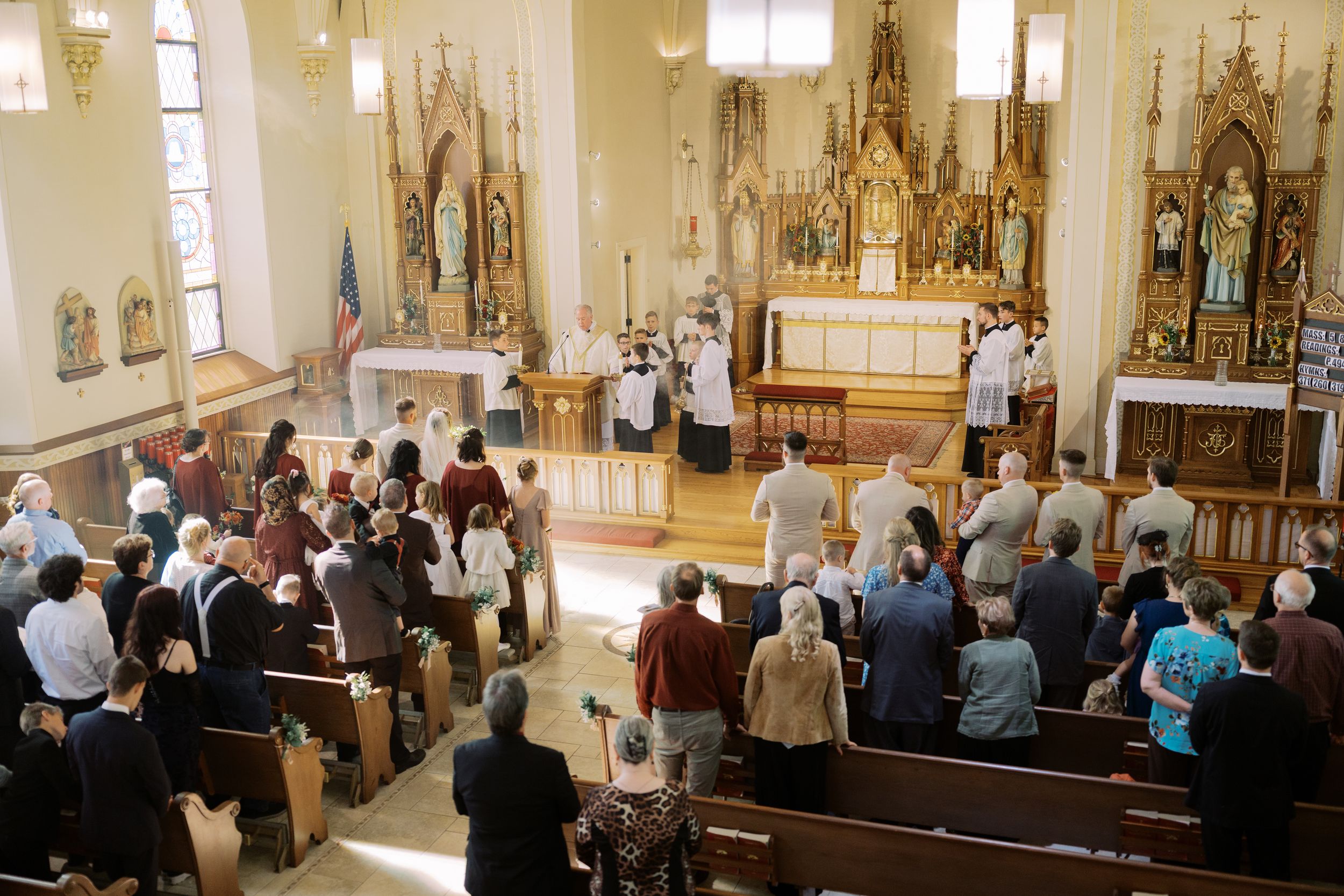 A panoramic view of a church interior with people standing in pews during a religious service.