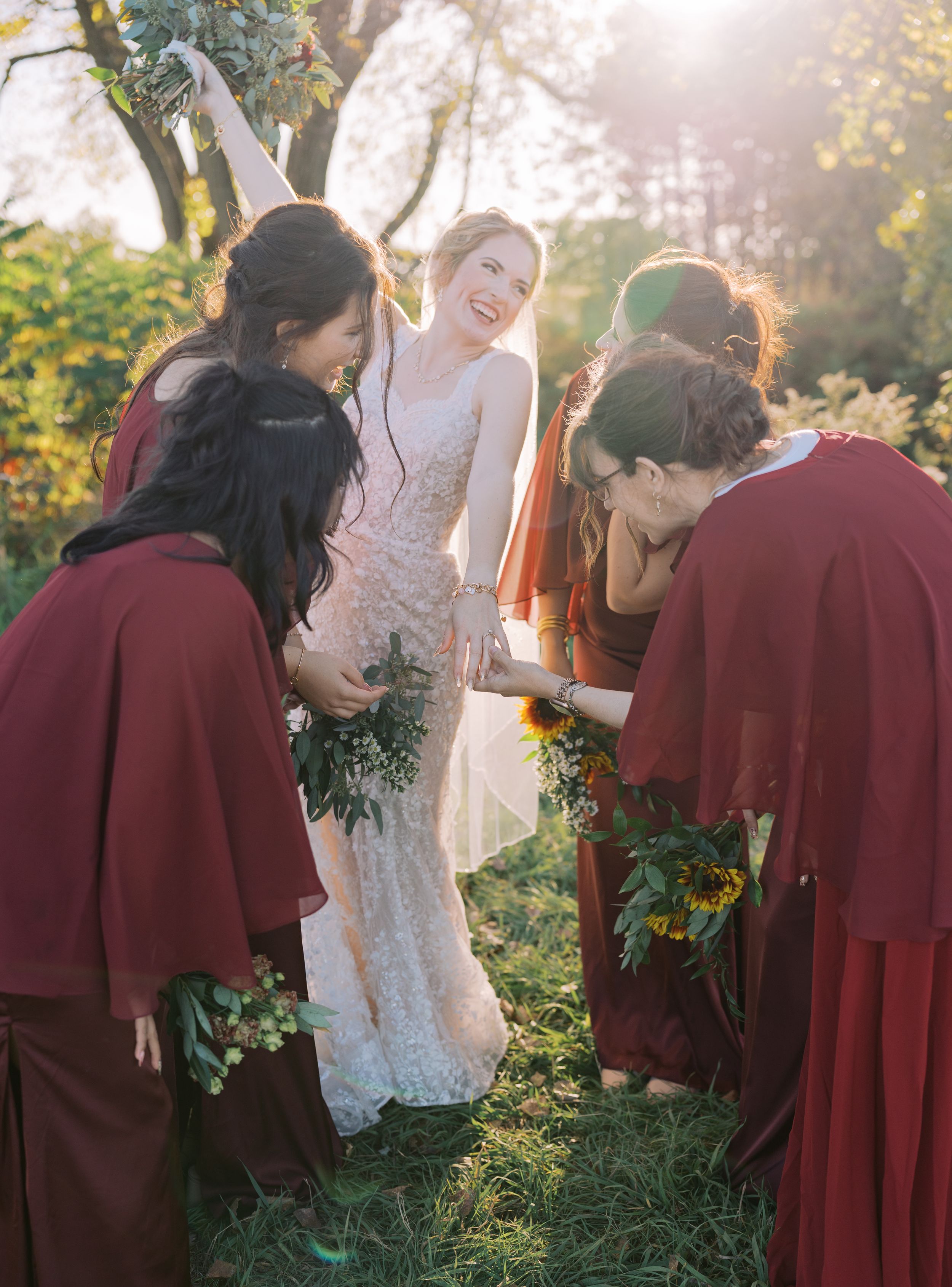 Wedding party in burgundy attire stands together in golden sunlight during an autumn outdoor ceremony.