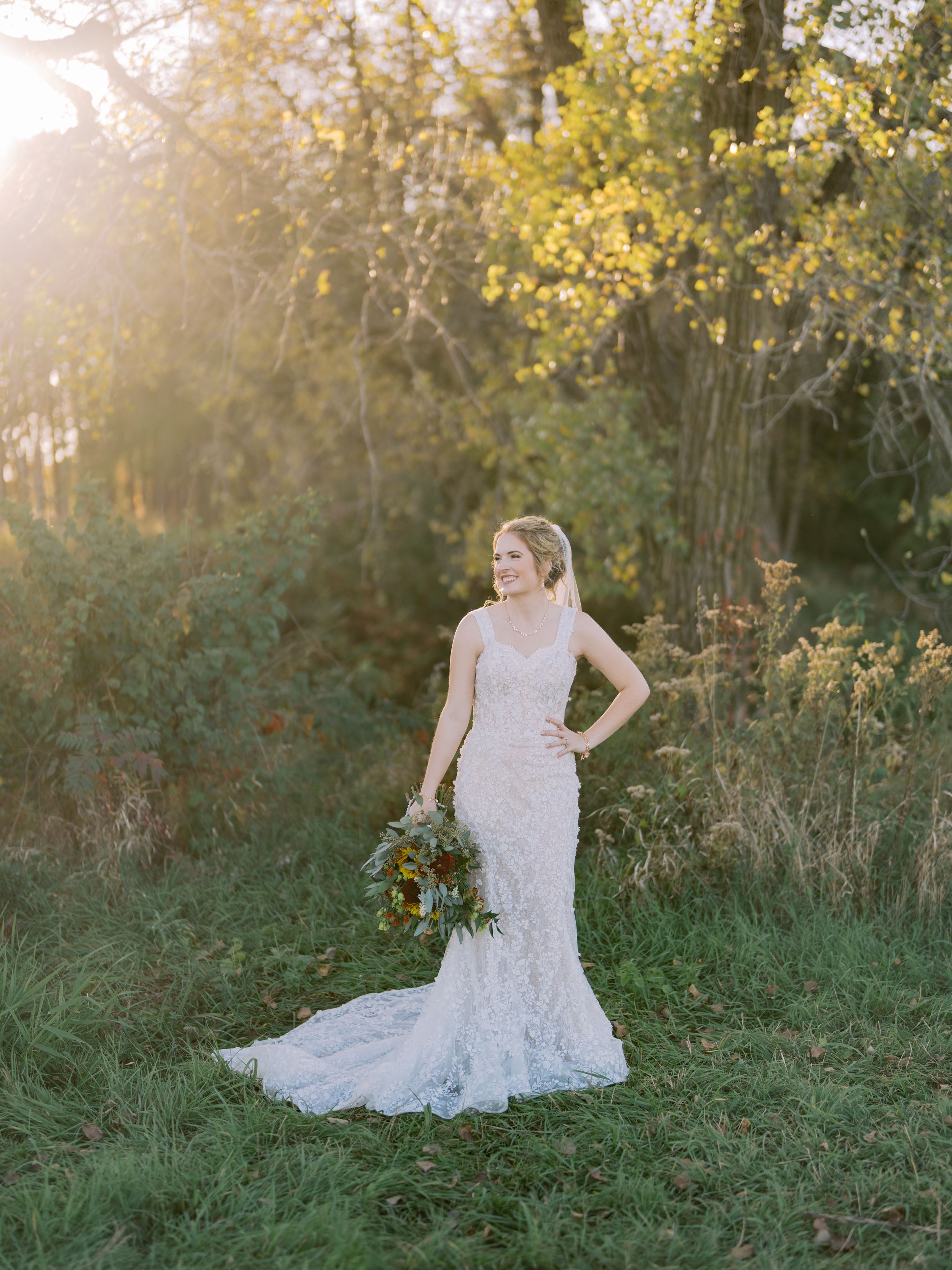 A person in a lace wedding dress poses gracefully in a sunlit meadow during golden hour.