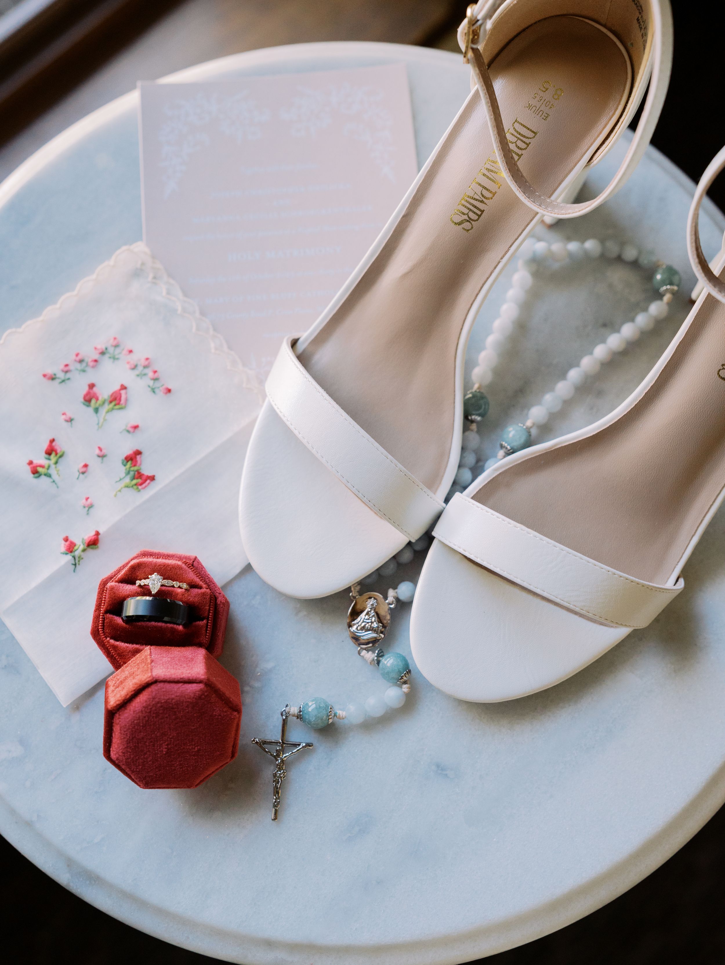 A series of white bridal shoes and red ring box arranged on a white surface showing wedding details and accessories.