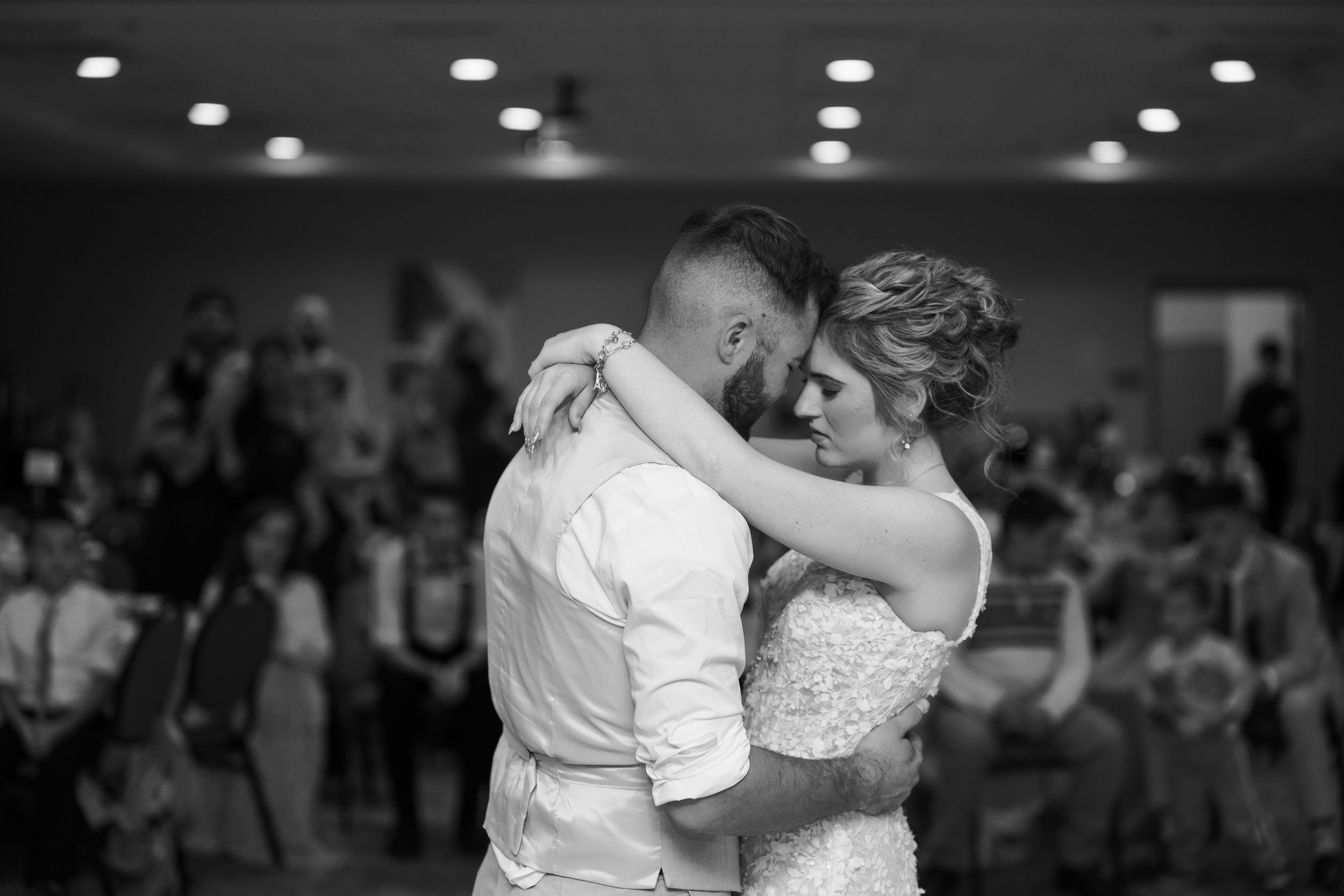 A couple shares their first dance at a wedding reception with guests watching in the background.