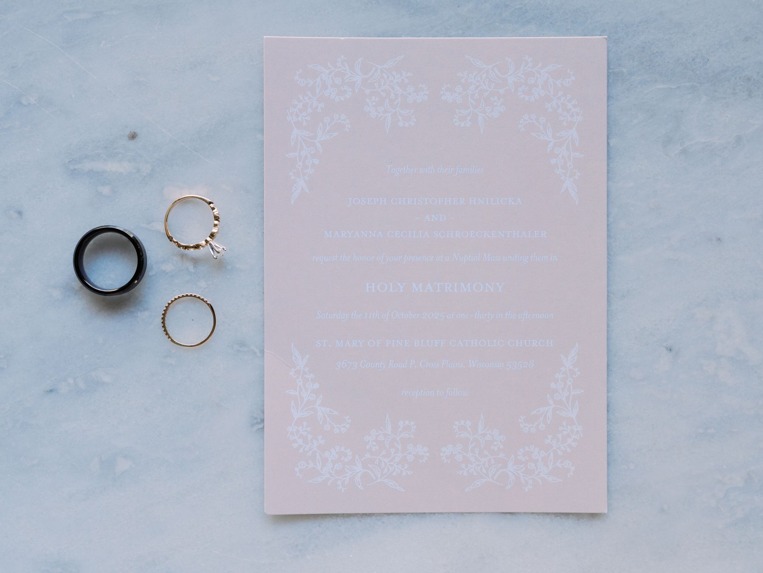 A series of light pink wedding invitations and stationery items arranged in a row against a blue marble background.