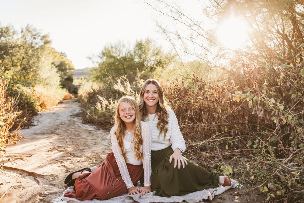 Two people in light colored tops sit together on a desert path during golden hour.
