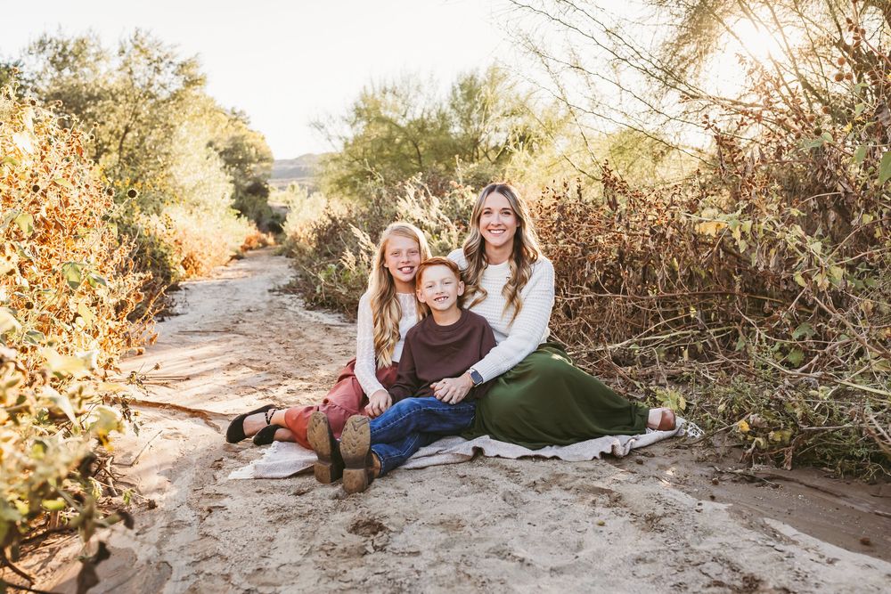 A family sits together on a dirt path surrounded by desert brush during golden hour.