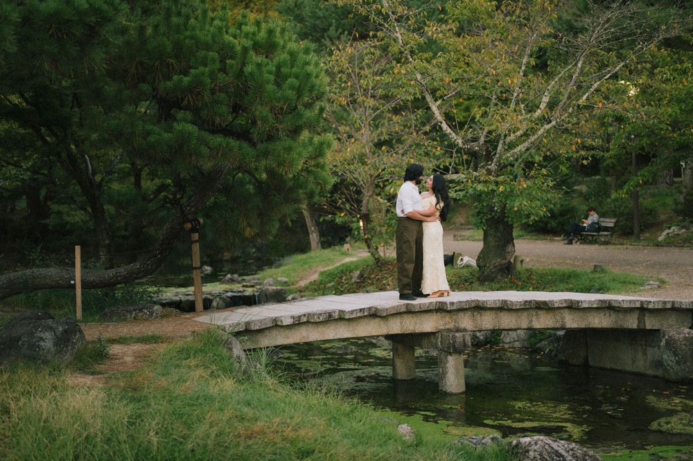 Couple standing close together on a rustic stone bridge over a tranquil pond in a Japanese garden.