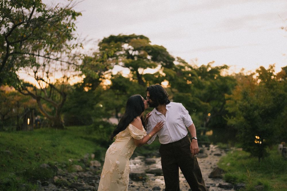Couple sharing a tender kiss near a rocky stream surrounded by green trees at dusk.