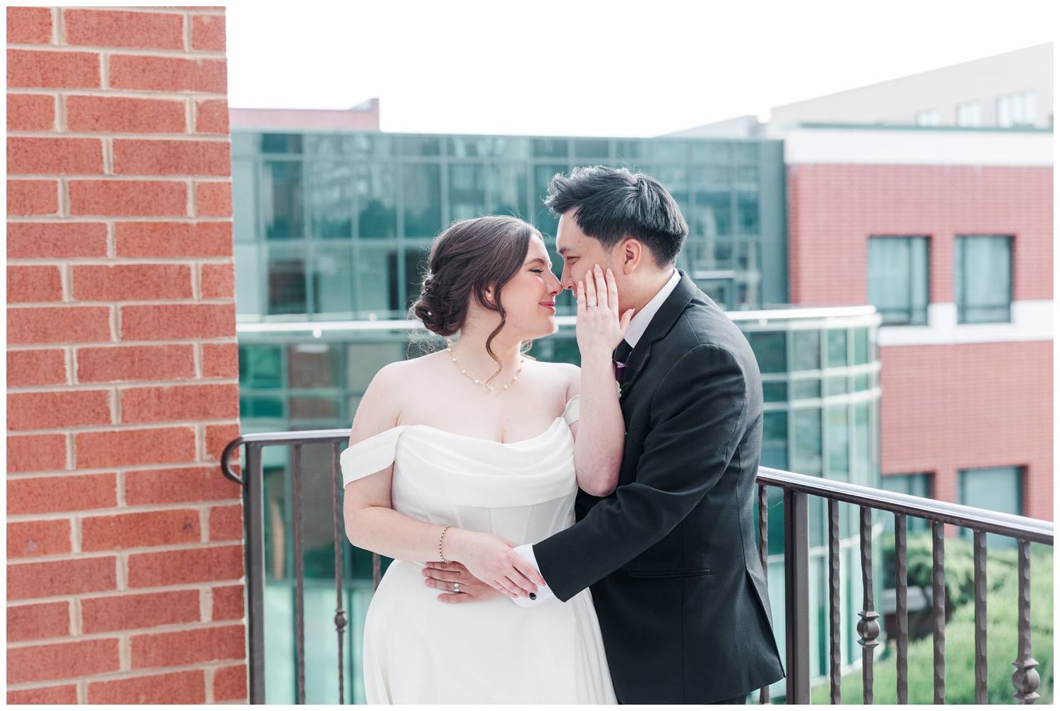 Romantic couple shares intimate moments against brick and glass building backdrop during wedding photoshoot.