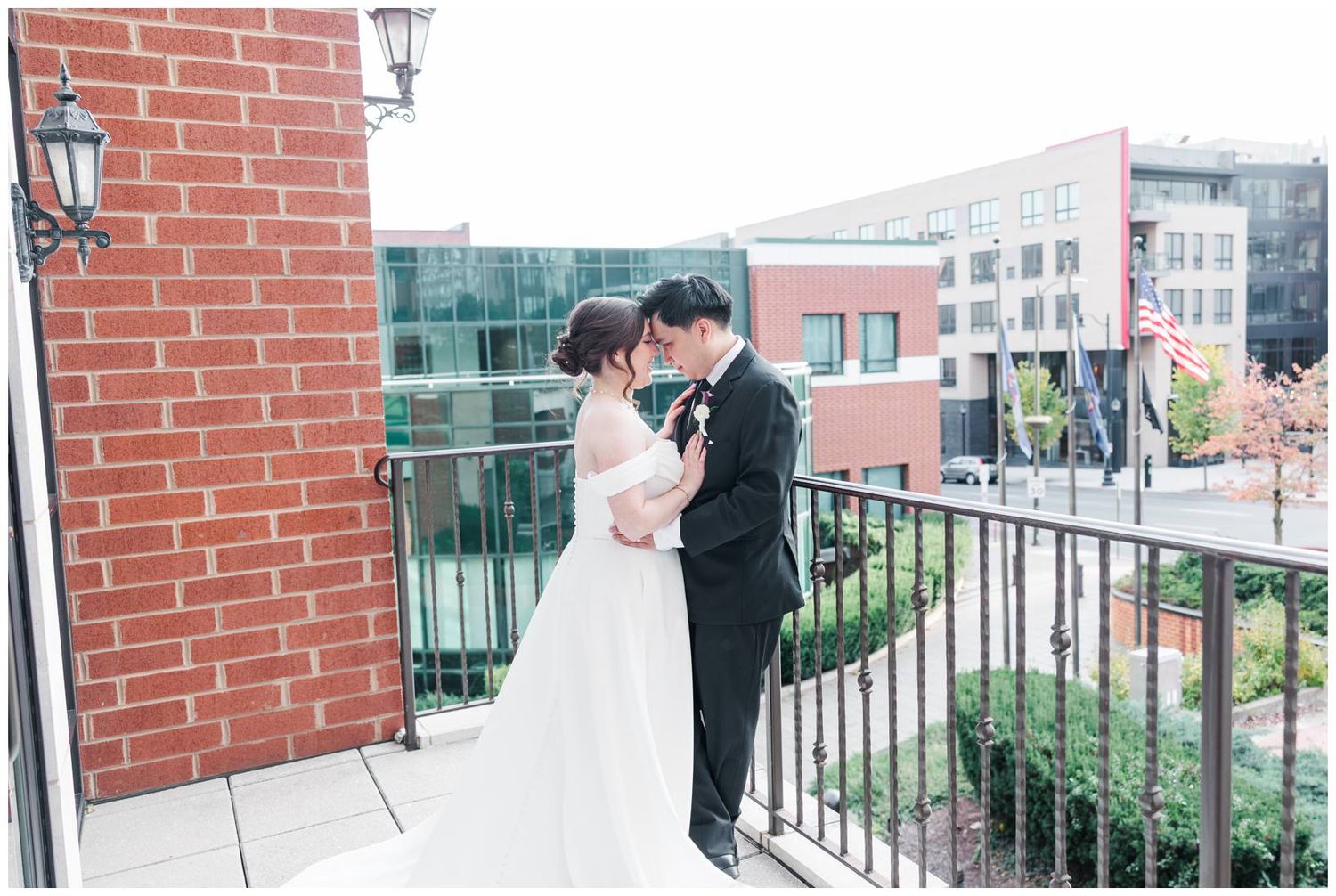 A couple shares a romantic moment on a brick balcony with city views and lantern lighting.