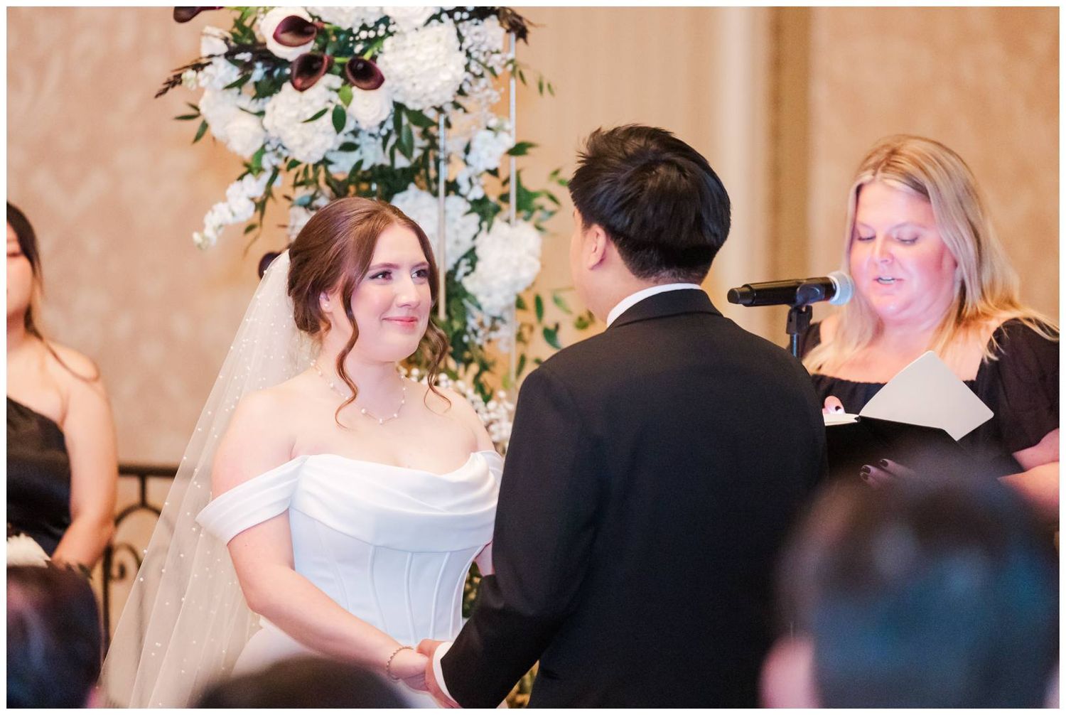 Wedding party members gather in an indoor venue with warm lighting and beige walls.