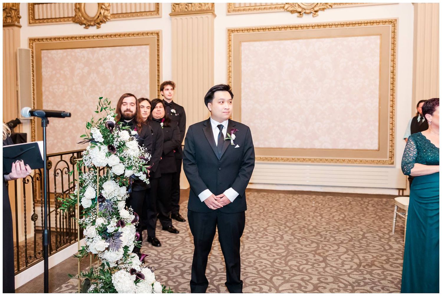 Wedding party members gather in an elegant ballroom with ornate decor and floral arrangements.