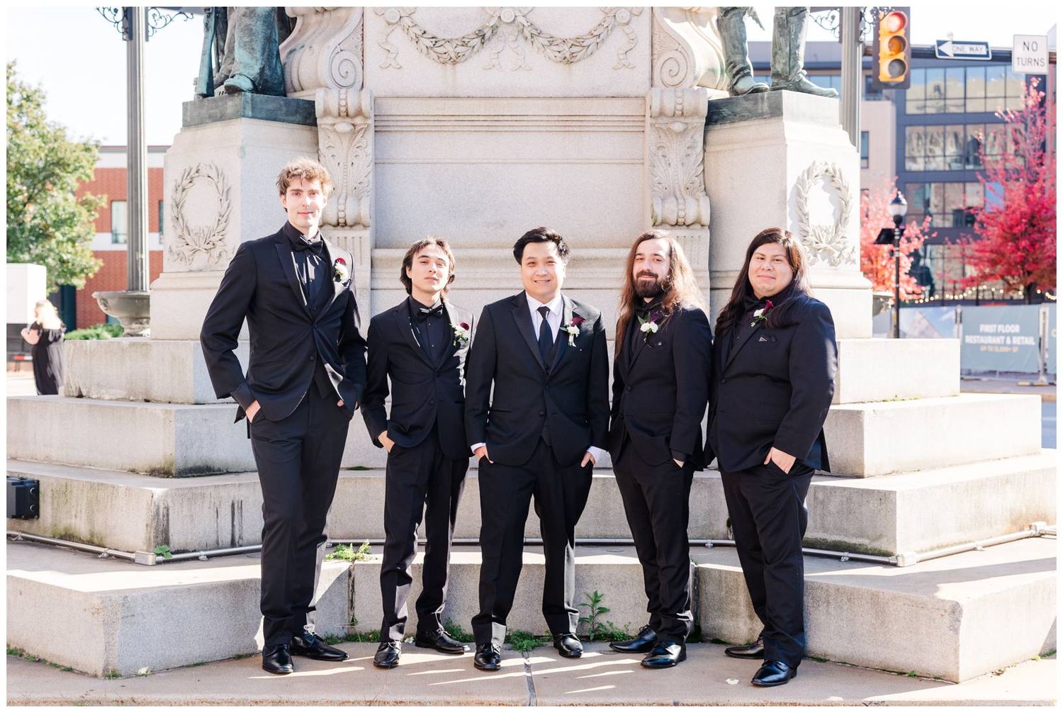 Wedding party members in black formal wear posing together against a stone building exterior.