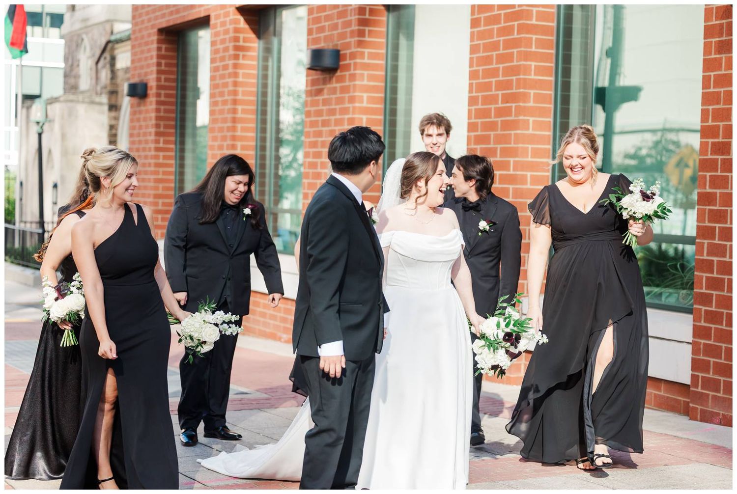 Wedding guests mingle and socialize outside a brick building during a daytime celebration.