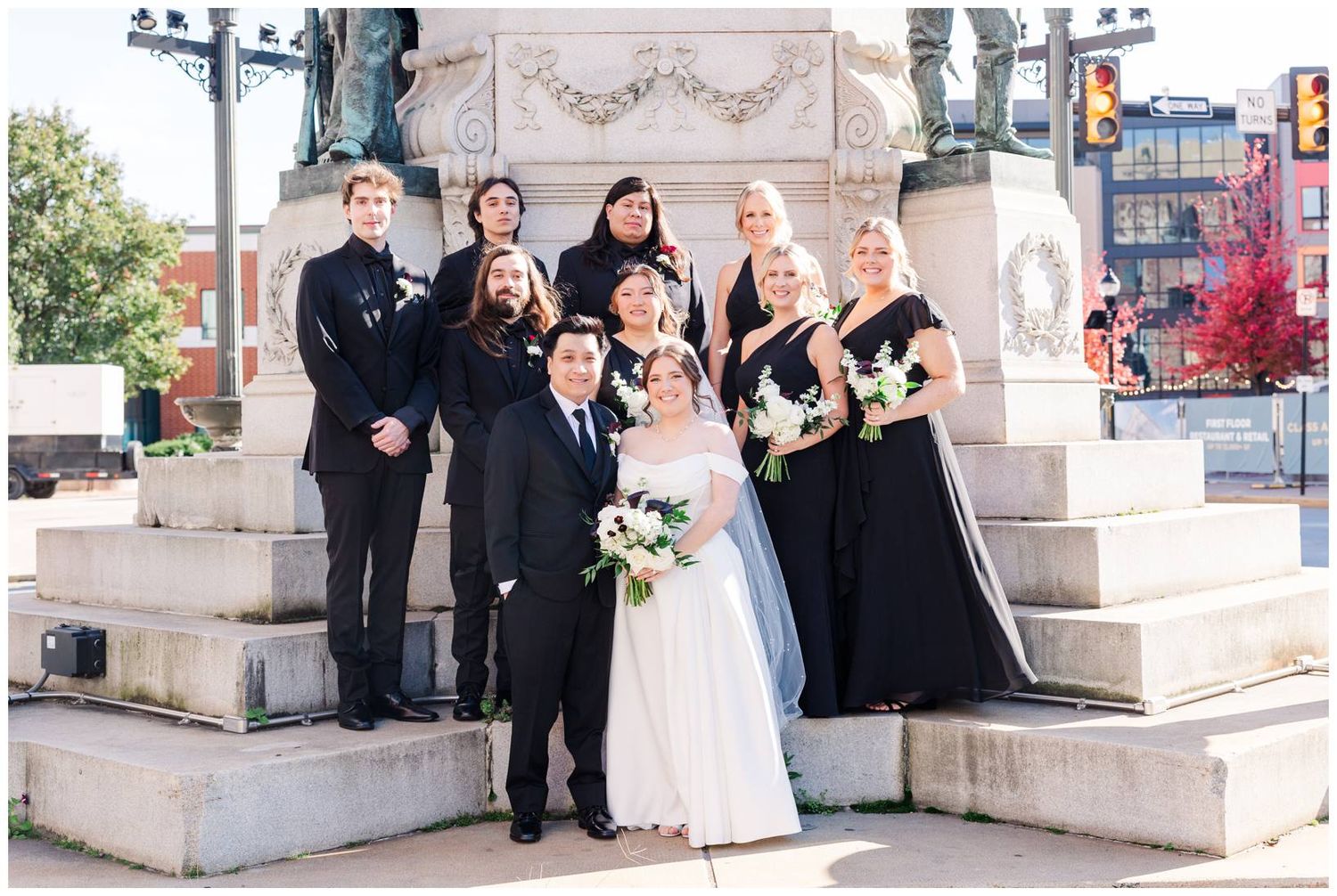 Wedding party gathered on stone monument steps for formal group photo.