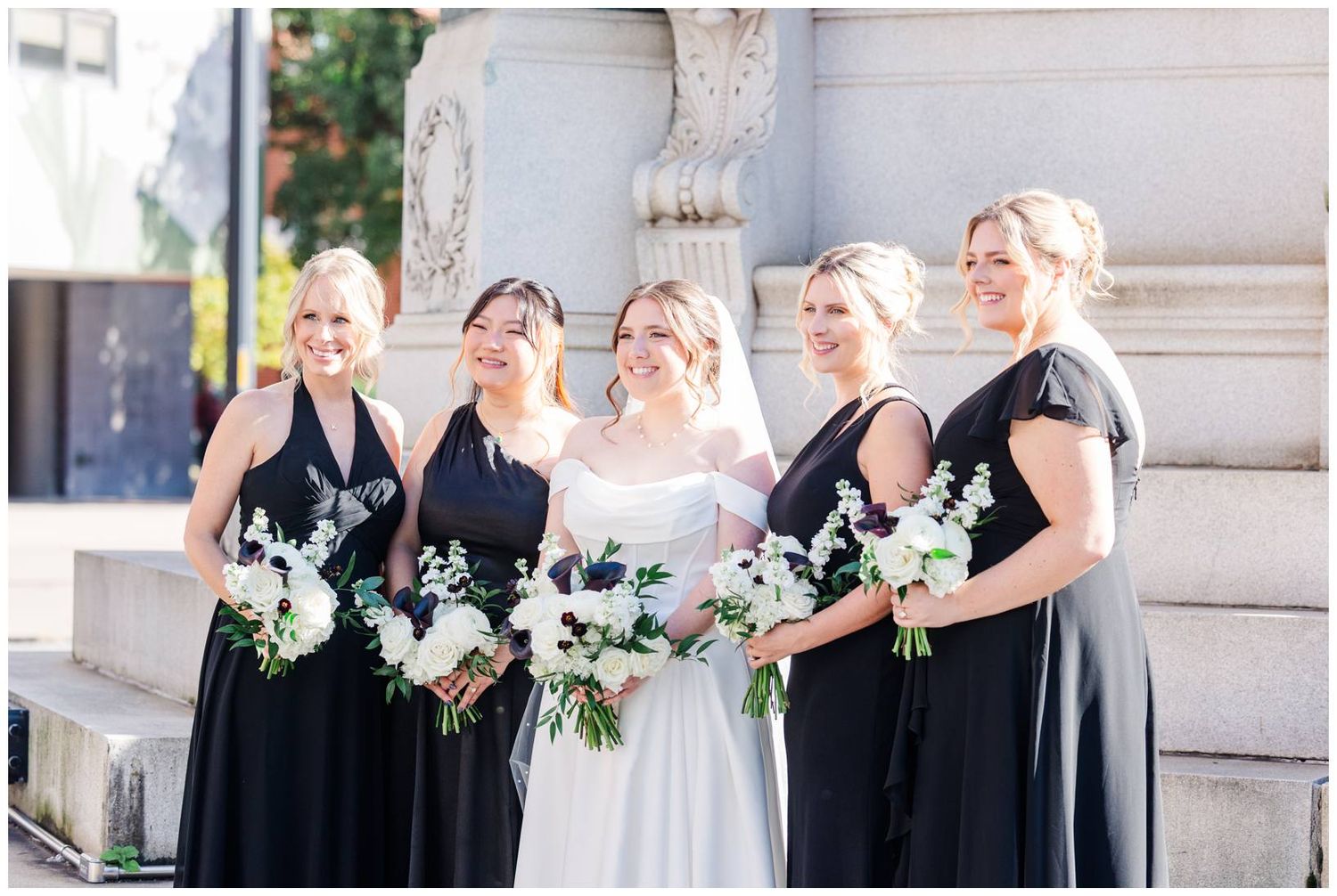 Wedding party in black dresses and formal attire gathered outdoors for formal portraits.