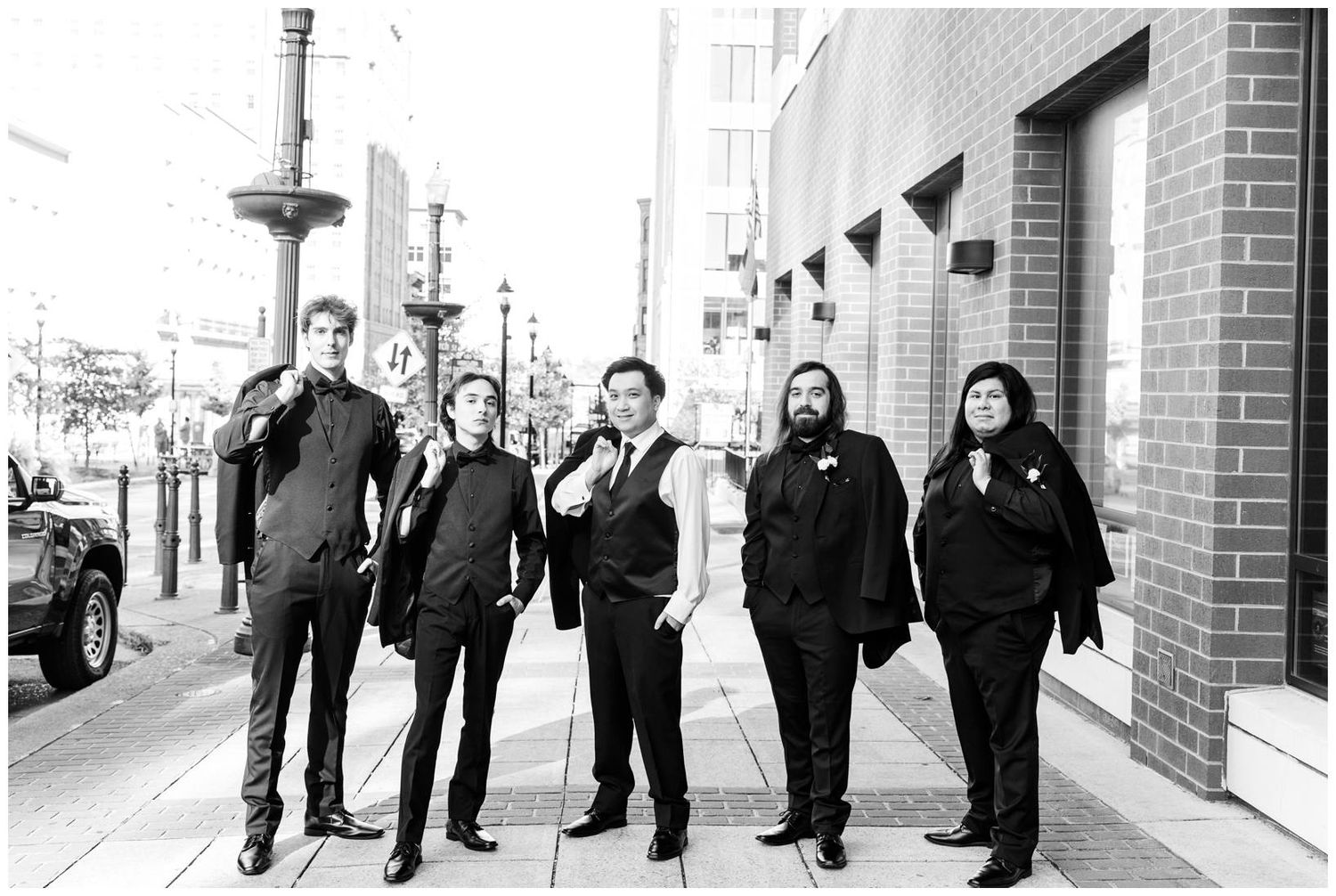 Wedding party members in formal attire stand outside brick building entrance.