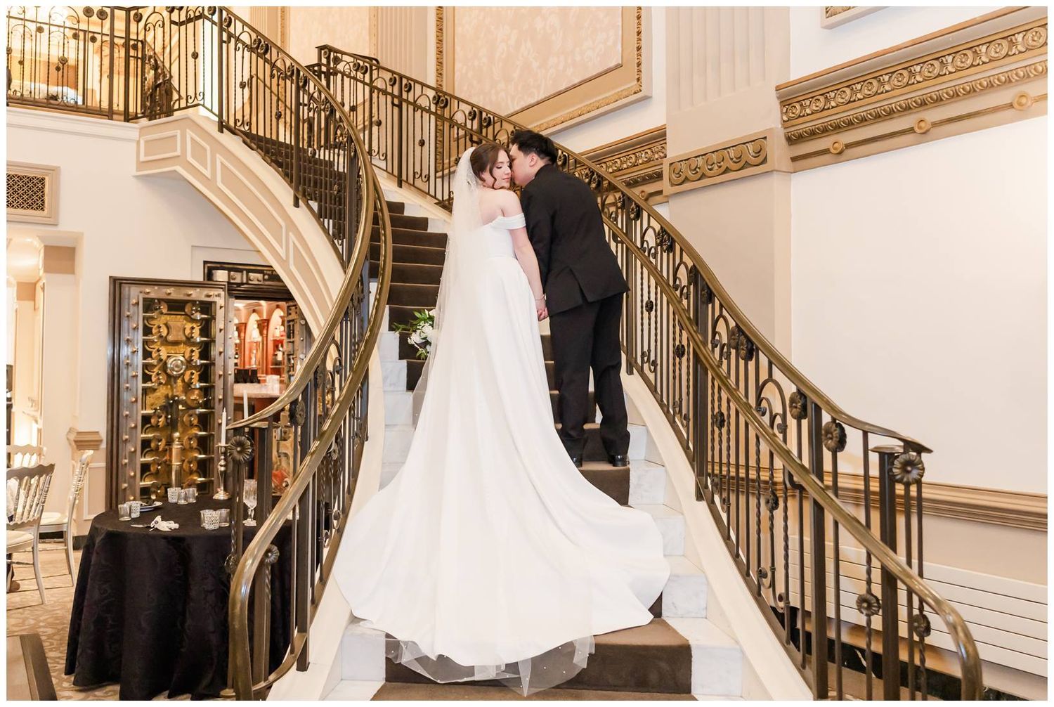 Elegant wedding party poses on grand staircase with ornate railings in luxurious venue.