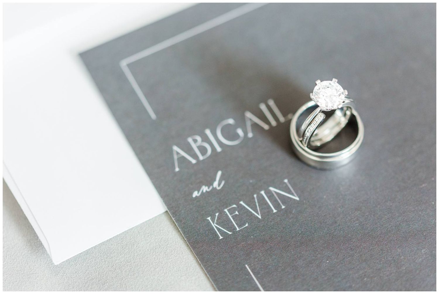 Close-up view of wedding rings resting on elegant black and white stationery with calligraphy text.