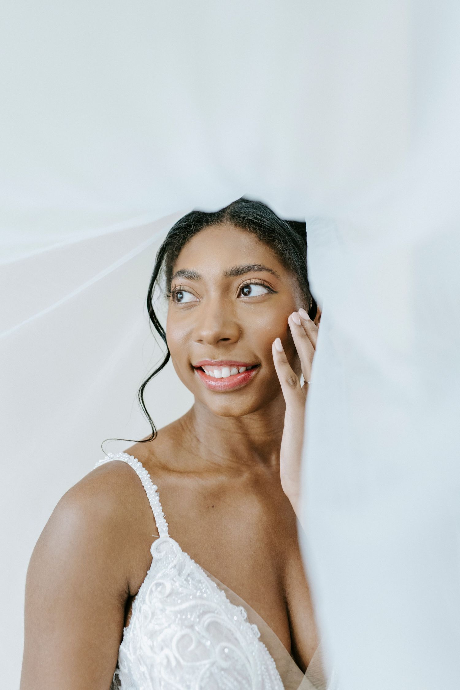 A bride in a white lace gown poses with joyful expressions against a bright background.