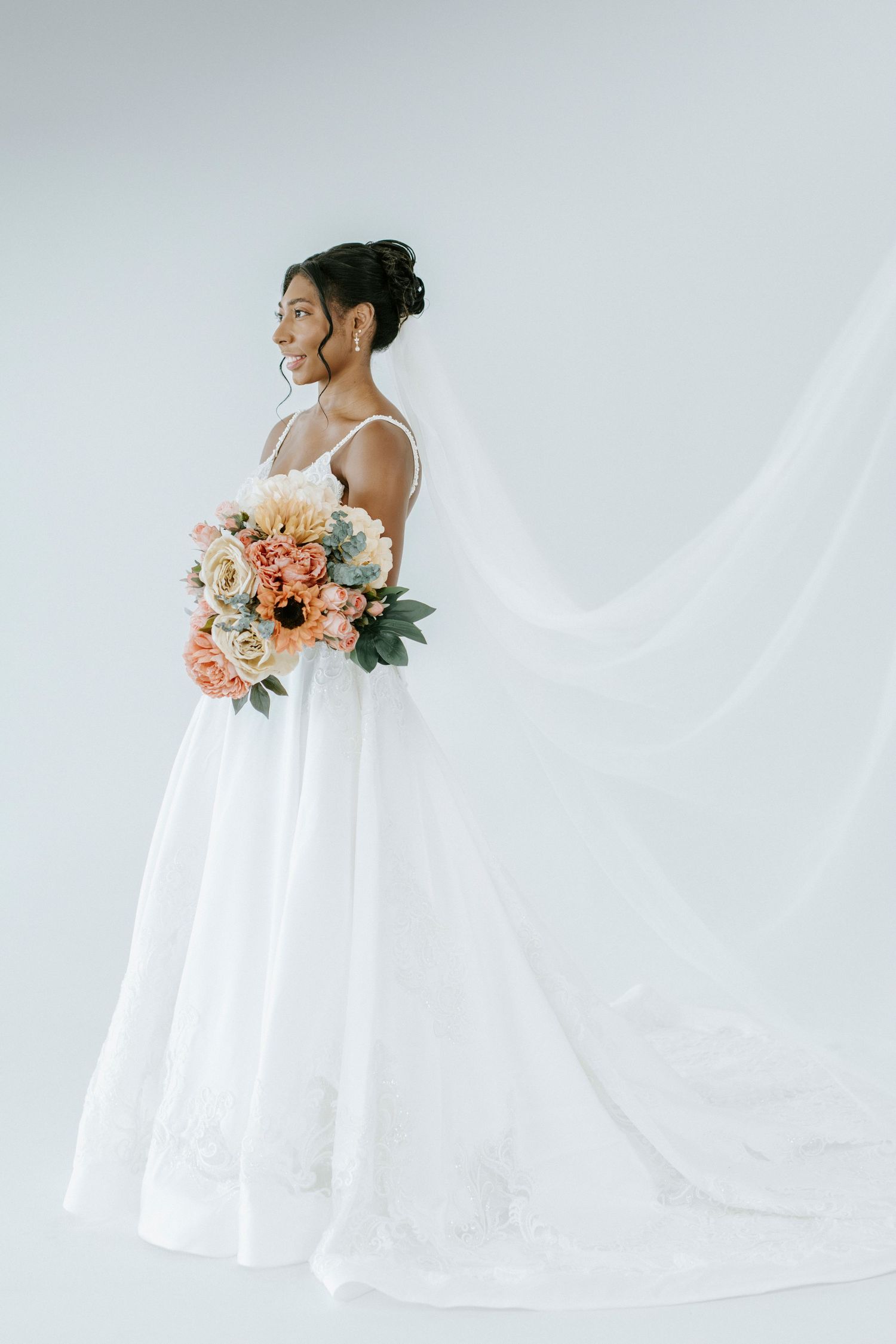 Minimalist bridal portrait featuring flowing white dress and peach-toned bouquet against white background.