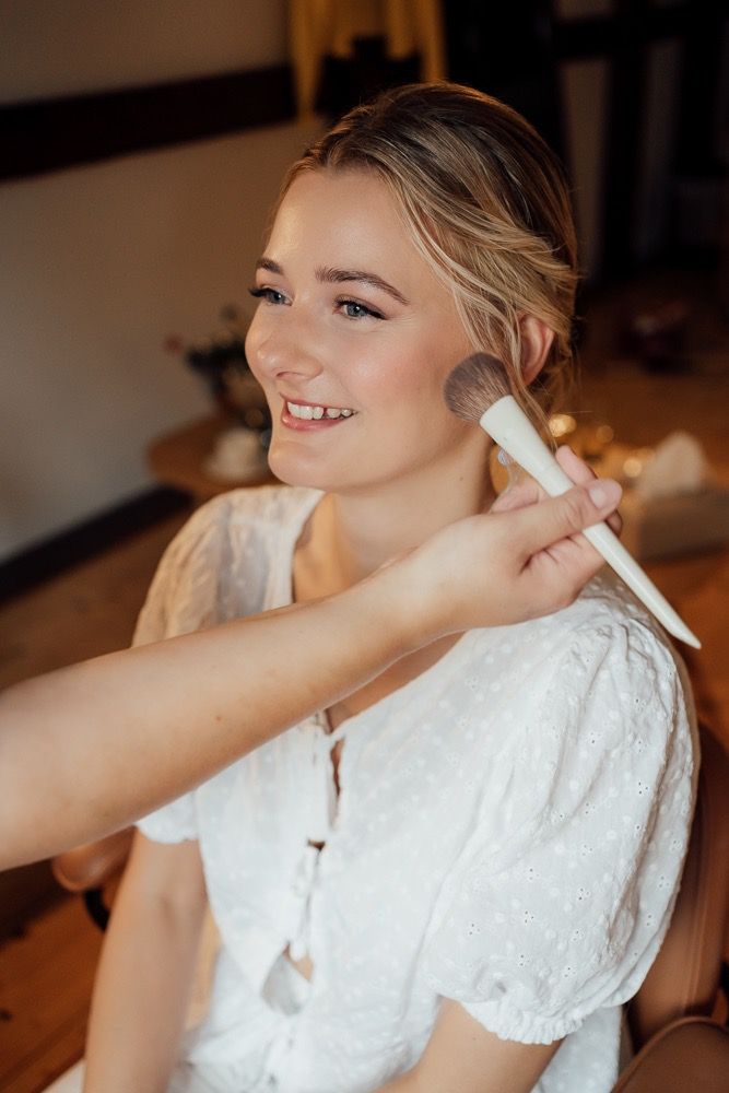 Wedding day preparation with makeup being applied to someone wearing a white lace dress.