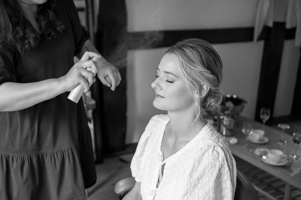 Wedding preparation scene showing hair and makeup styling in a rustic room.