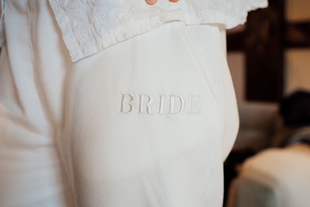 Close-up detail of white bridal robe with embroidered 'BRIDE' text.