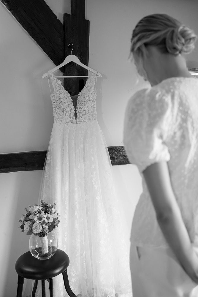 White lace wedding dress hanging on display with soft natural lighting in a dressing room.