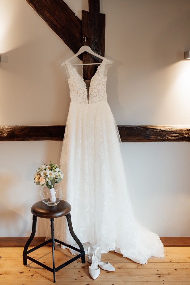 White lace wedding dress hanging on display against a wall with wooden beams.