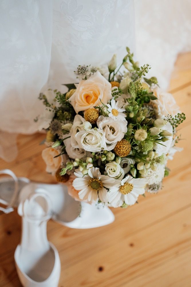 Wedding bouquet with white and peach roses arranged with golden accents on a wooden surface.