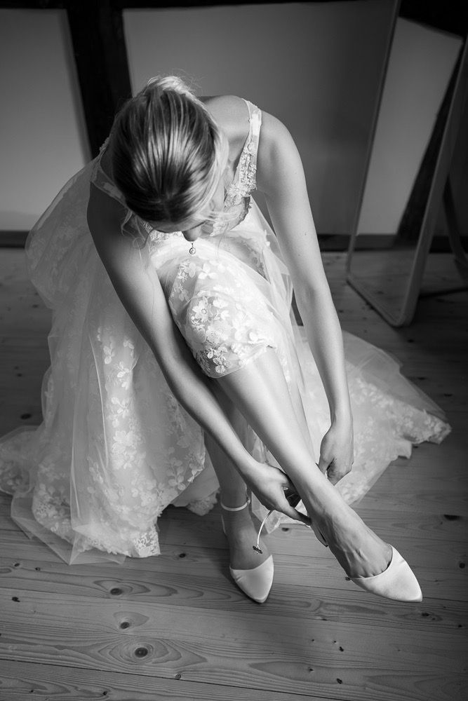 A series of black and white photos showing someone putting on white bridal shoes with a lace dress.