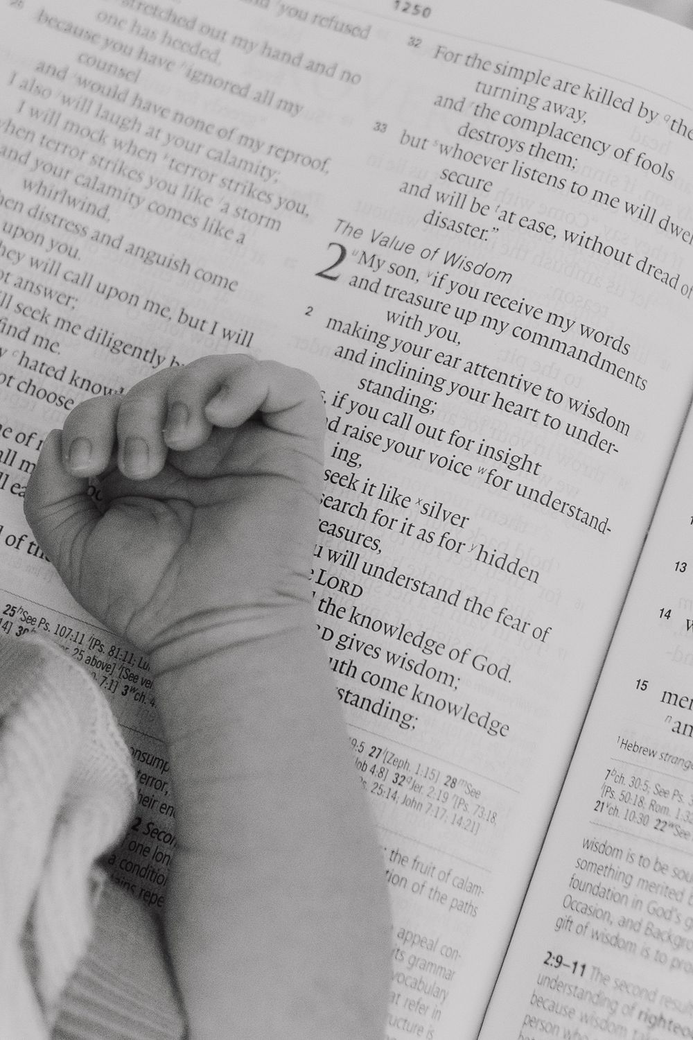 A tiny baby's foot rests on an open Bible page in black and white.