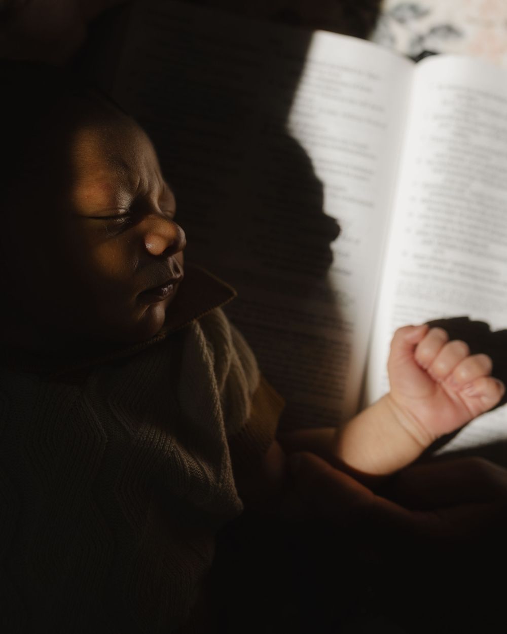 Someone reading a book in low light conditions with pages illuminated against a dark background.