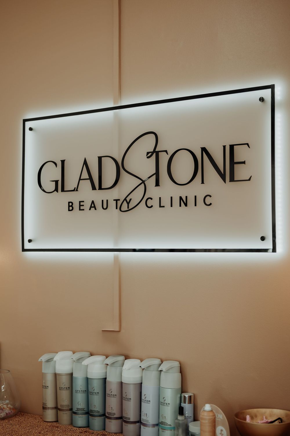 Elegant 'Gladstone Beauty Clinic' signage displayed on a neutral-toned wall with product shelves below.