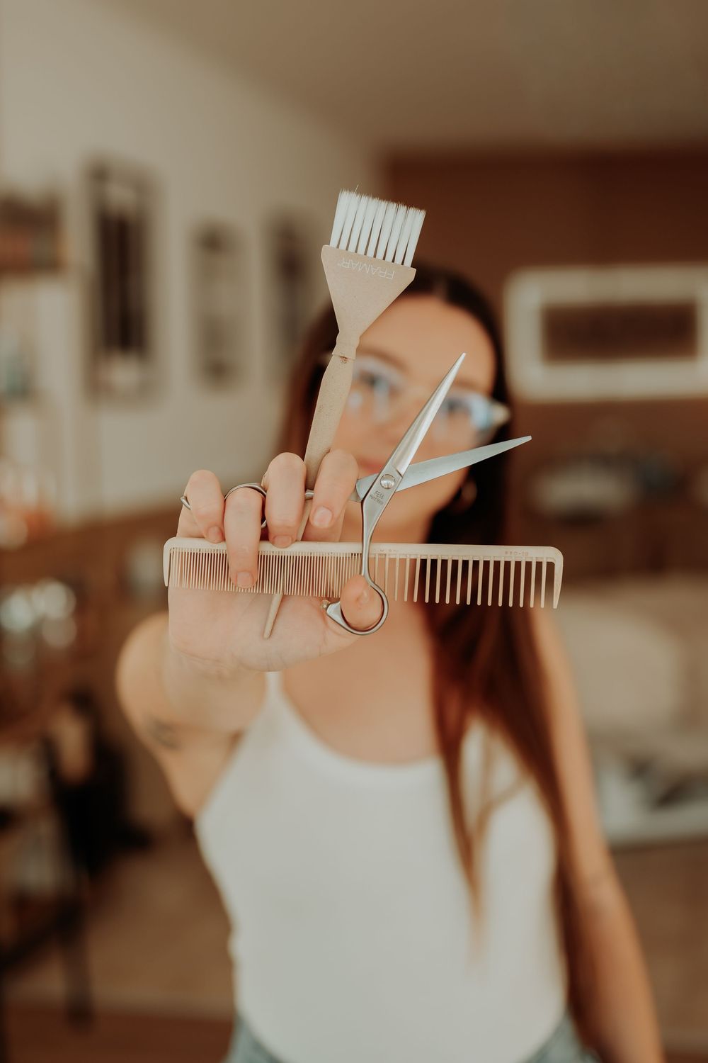Close-up of hairdressing tools including scissors and combs held against warm lighting.
