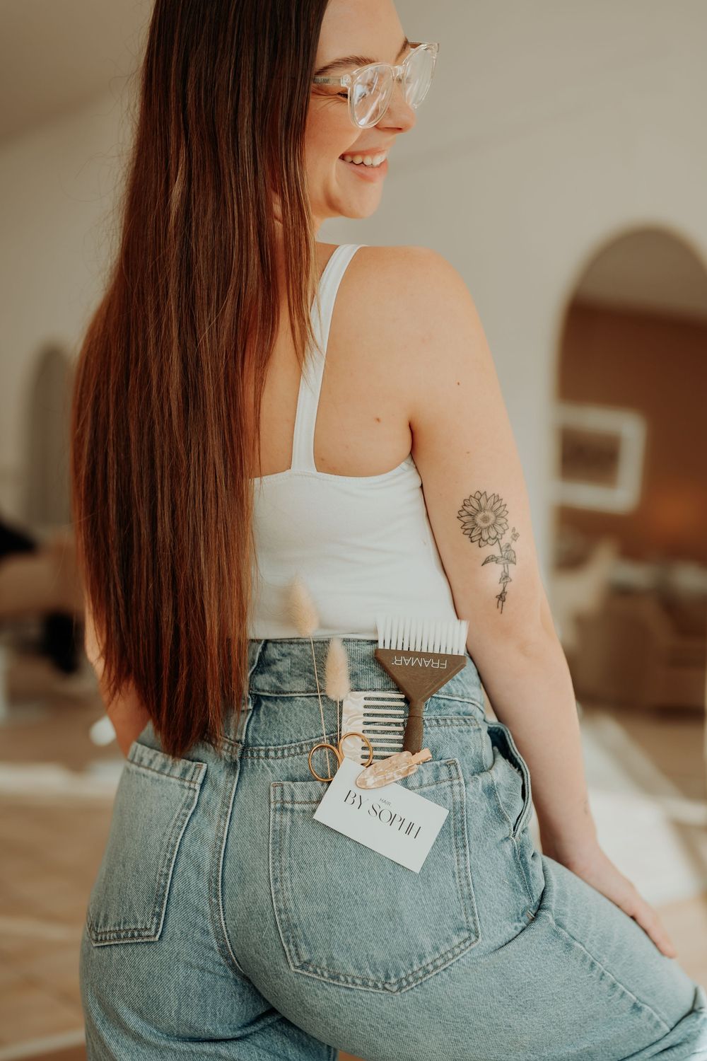 Back view showing high-waisted denim jeans and white tank top in a salon setting.