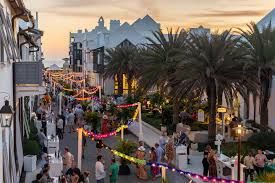 Tourists stroll through a charming Mediterranean coastal town at sunset with palm trees lining the cobblestone street.