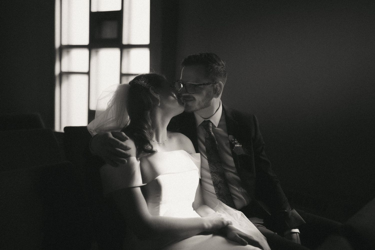 A person works at a dimly lit desk with a bright window casting dramatic lighting in a moody black and white scene.