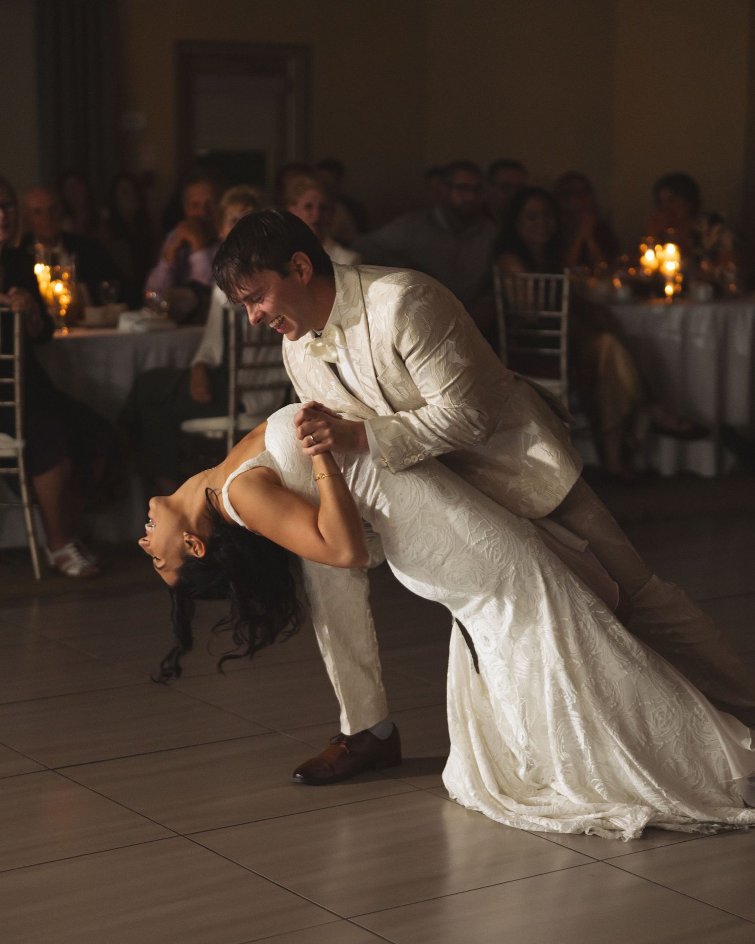 A couple performs a dramatic dip during their first dance at a dimly lit wedding reception.