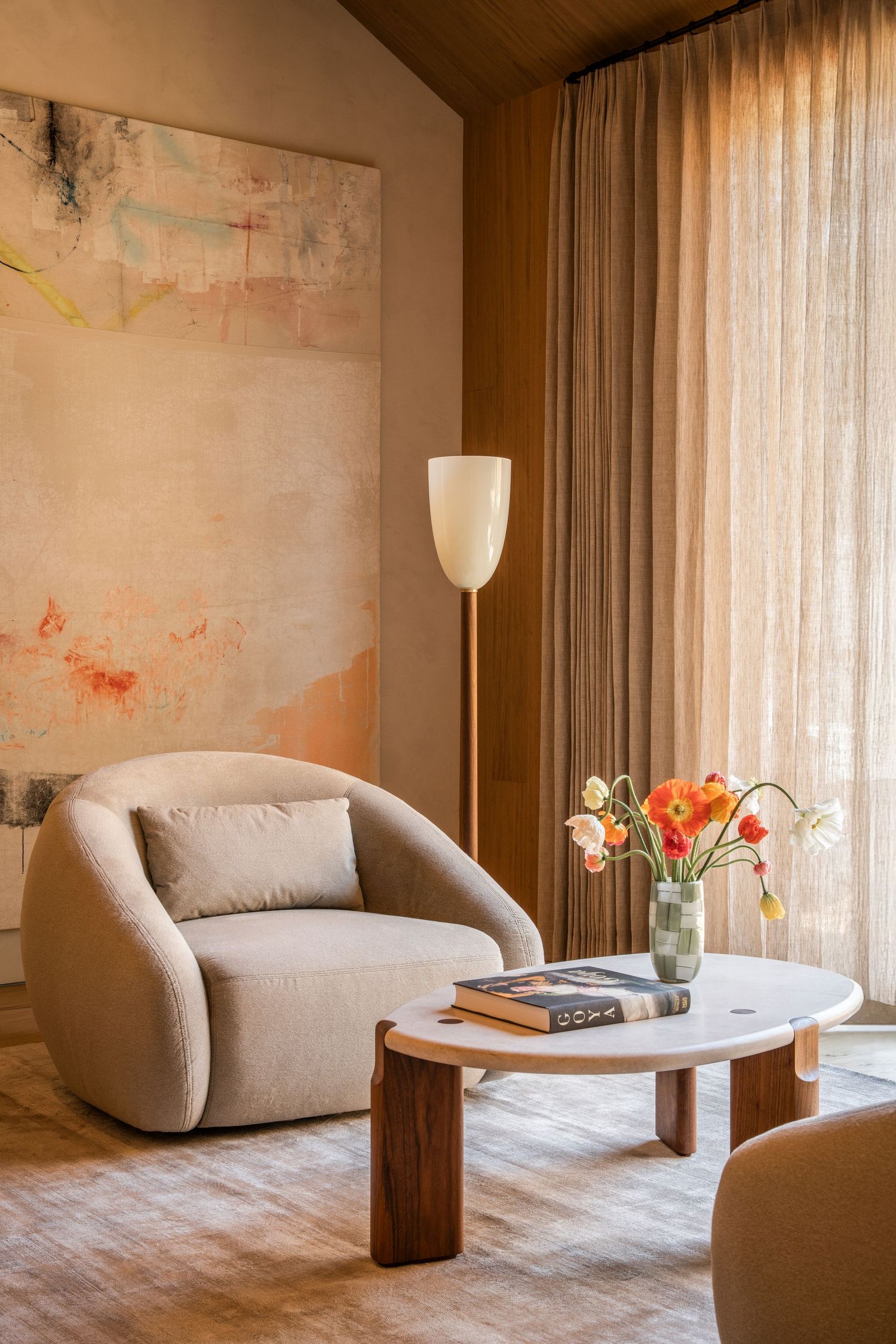 Modern living room interior with curved beige sofa, white round coffee table and floor lamp against textured wall.