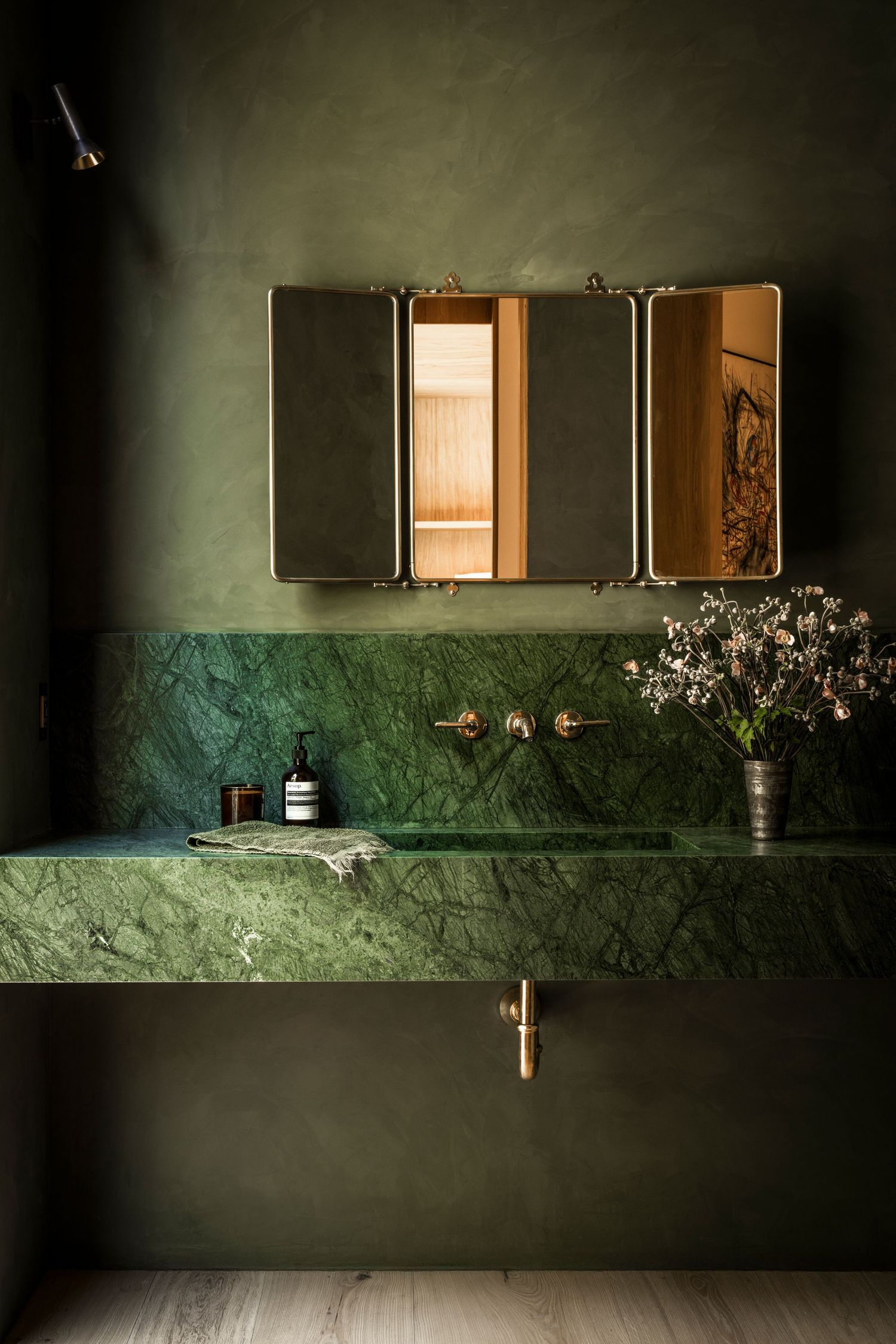Sleek modern bathroom with green marble walls featuring minimalist medicine cabinets and delicate floral arrangements.