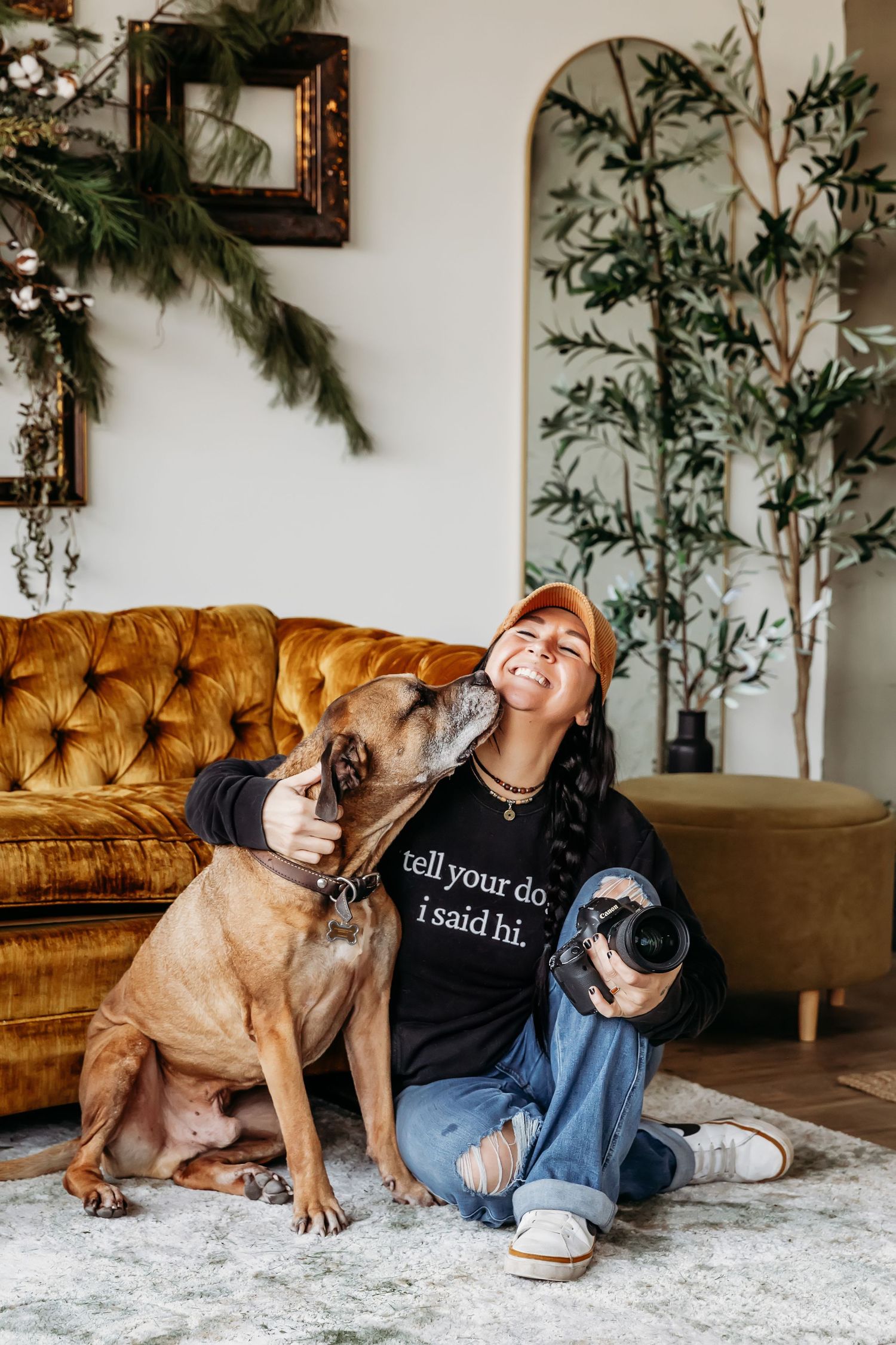 Casual indoor photoshoot with dogs beside decorative plant wall and tufted sofa.