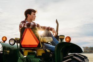 A person drives a vintage tractor across a rural field at sunset while silhouetted against the golden sky.