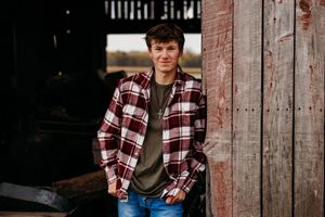 Person in plaid flannel shirt poses against rustic wooden barn wall in outdoor portrait series.