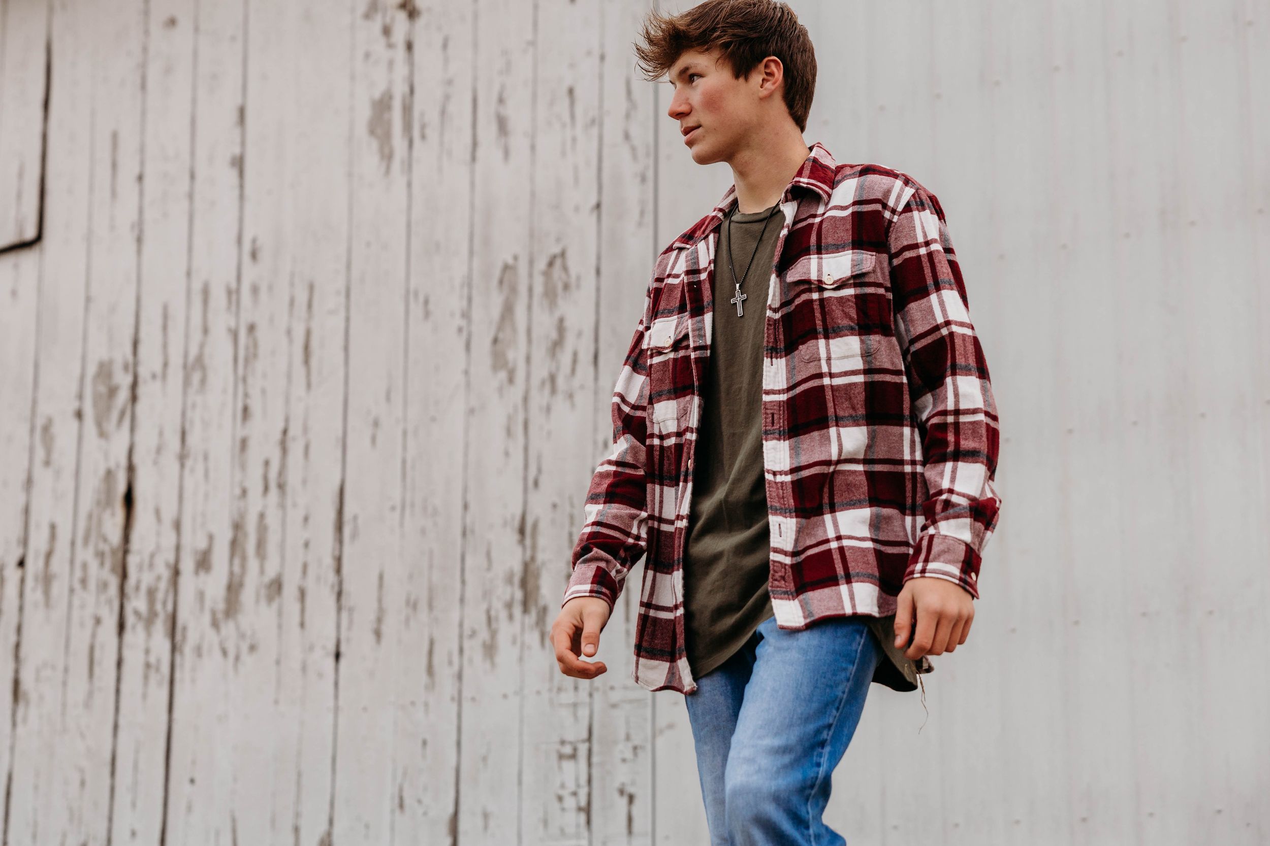 Two people in casual fall attire laugh and walk together in front of a white wooden wall.