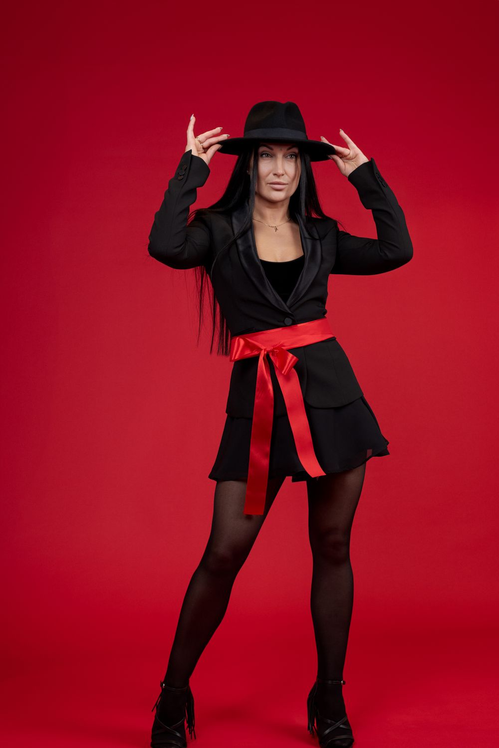 Stylish figure in black attire and hat posing dramatically against red backdrop.