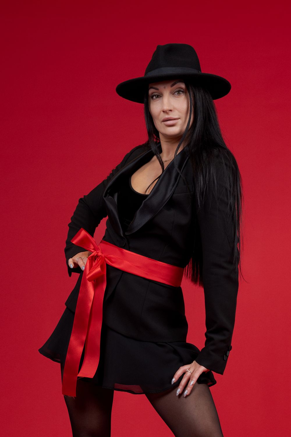 Fashion model in black outfit with red bow accent strikes poses against red background.