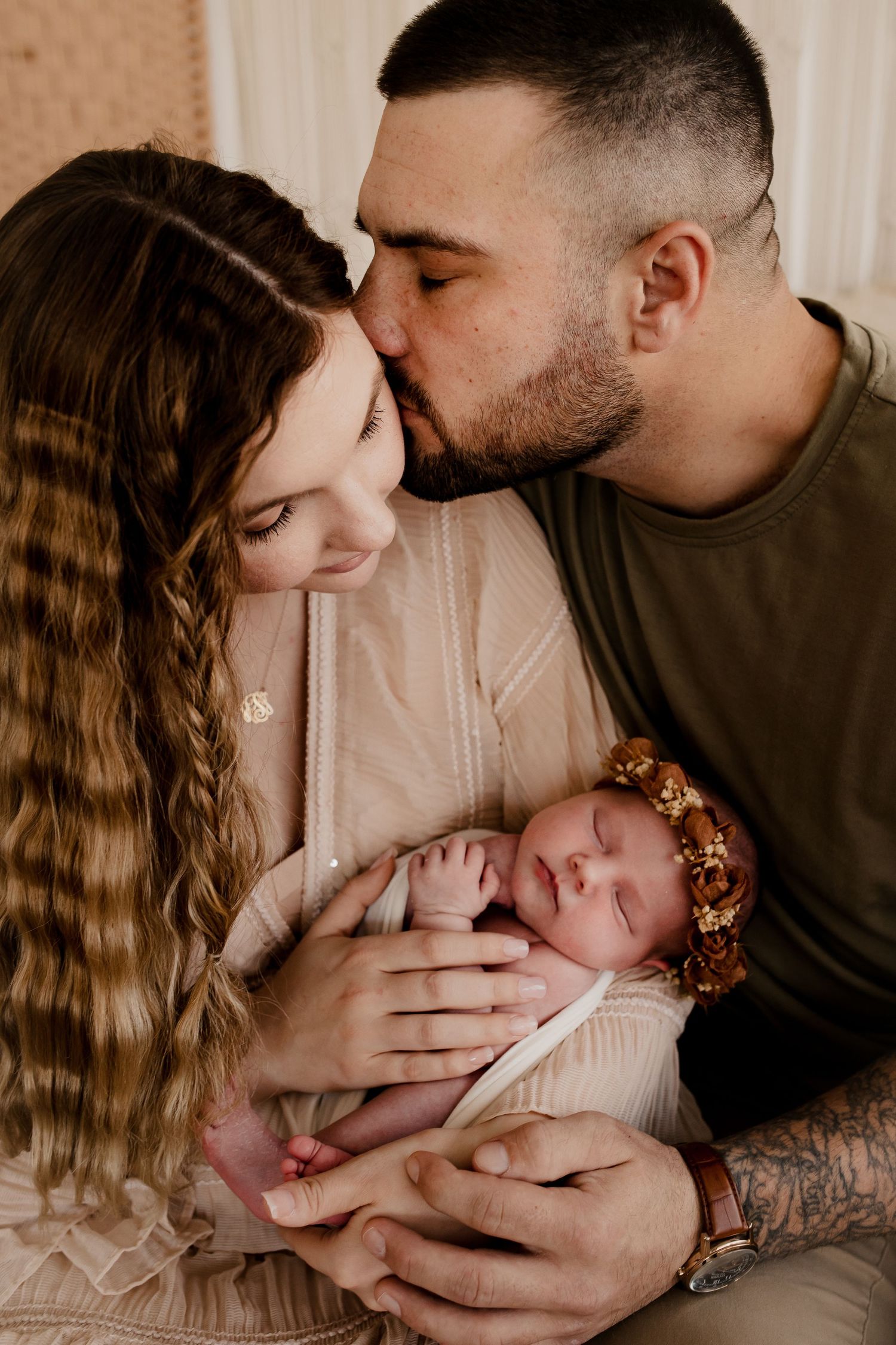 Dad kissing mother as she holds their newborn baby during a luxury studio newborn session in St. Louis.